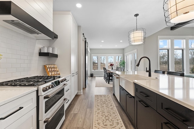 kitchen featuring light wood finished floors, range with two ovens, light countertops, premium range hood, and stainless steel dishwasher