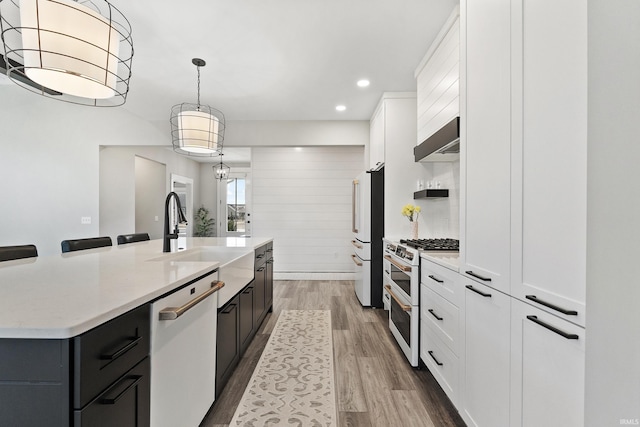 kitchen with wood finished floors, exhaust hood, high quality appliances, white cabinets, and light countertops