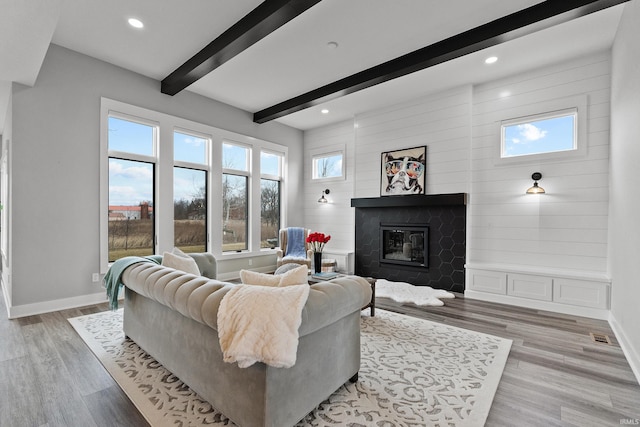 living room with light wood-style floors, a glass covered fireplace, beamed ceiling, and baseboards