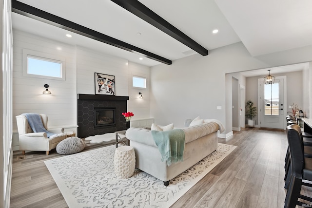 living area with light wood-style flooring, baseboards, beamed ceiling, and a glass covered fireplace