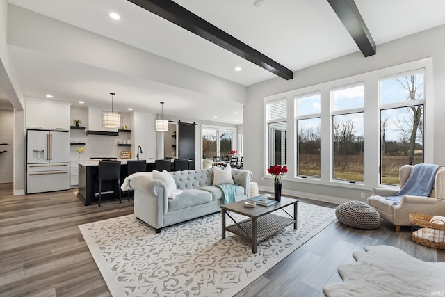 living area with light wood-type flooring, a healthy amount of sunlight, beamed ceiling, and baseboards