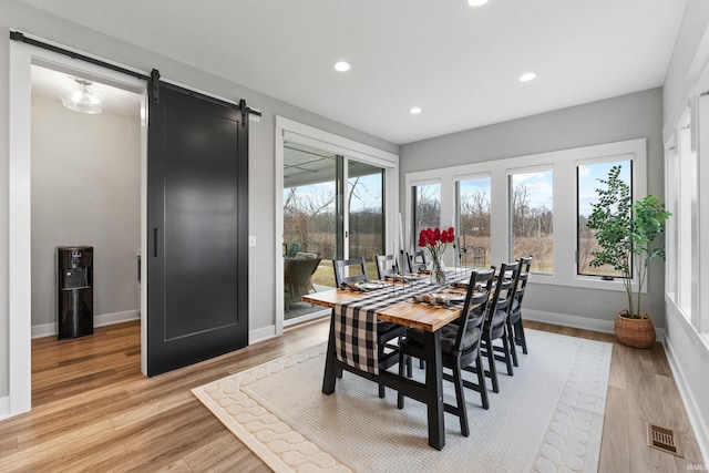 dining space with a healthy amount of sunlight, visible vents, light wood-style flooring, and a barn door