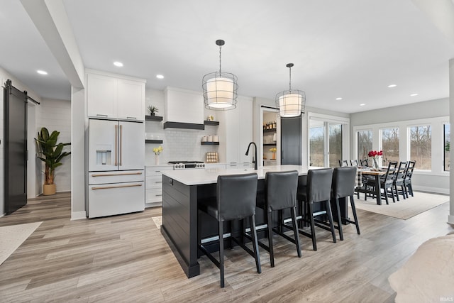 kitchen featuring high end white refrigerator, a barn door, decorative backsplash, light wood-style flooring, and light countertops