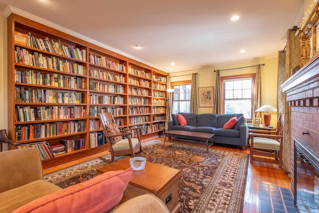 living area with hardwood / wood-style flooring, ornamental molding, wall of books, a fireplace, and recessed lighting