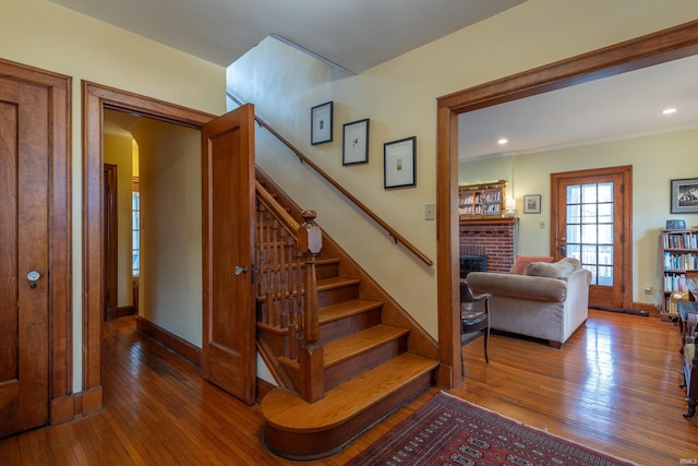 stairway featuring baseboards, recessed lighting, wood-type flooring, and a brick fireplace