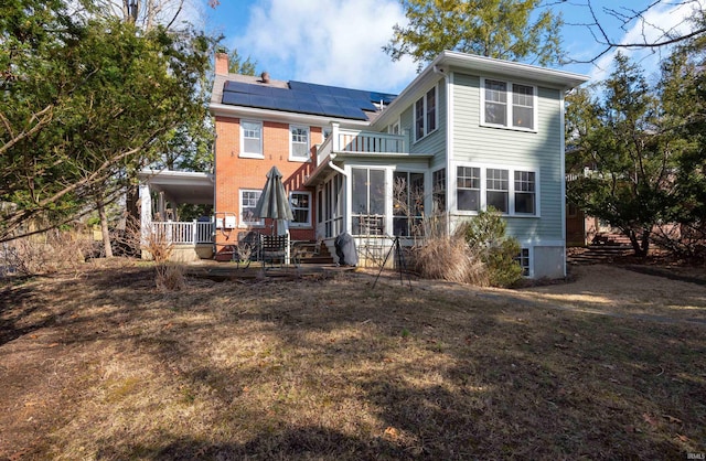 back of property featuring a sunroom, a chimney, and roof mounted solar panels