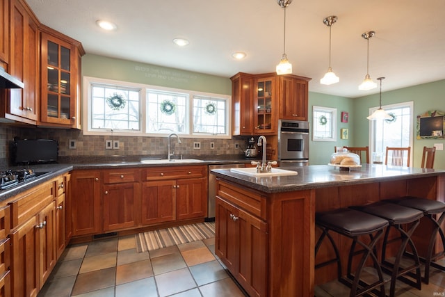 kitchen with a breakfast bar area, brown cabinets, stainless steel appliances, and a sink