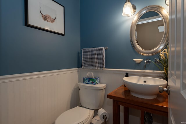 half bathroom with a sink, toilet, and wainscoting