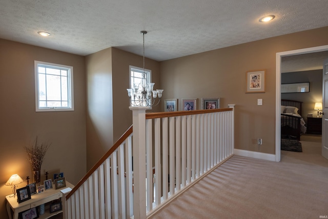 corridor with baseboards, carpet, a chandelier, an upstairs landing, and a textured ceiling