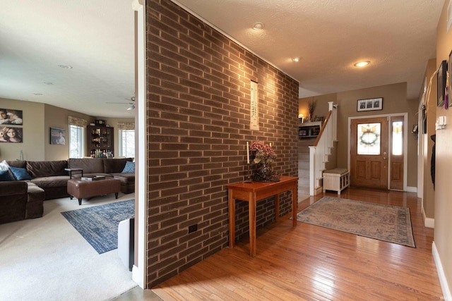 entrance foyer featuring a textured ceiling, stairway, brick wall, light wood finished floors, and baseboards