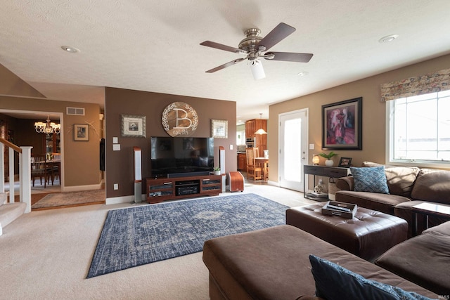 carpeted living area featuring baseboards, visible vents, stairs, a textured ceiling, and ceiling fan with notable chandelier