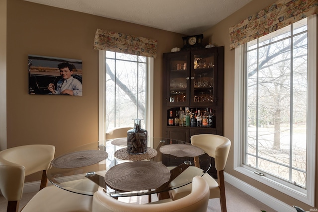 dining space featuring a textured ceiling, a bar, and baseboards