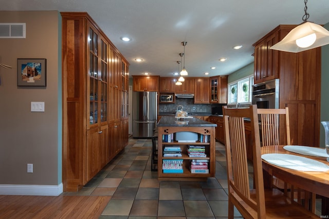 kitchen with visible vents, stainless steel appliances, under cabinet range hood, brown cabinets, and backsplash