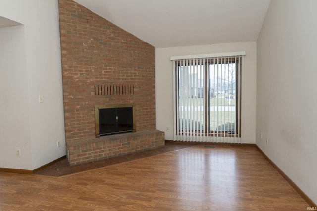 unfurnished living room with vaulted ceiling, a brick fireplace, wood finished floors, and baseboards