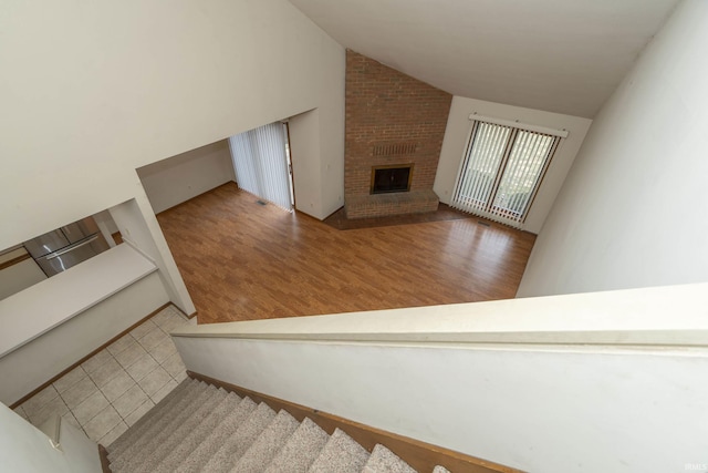 stairs with a brick fireplace, high vaulted ceiling, and wood finished floors