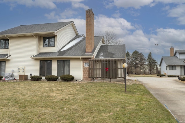 view of front of home featuring roof with shingles, brick siding, a chimney, concrete driveway, and a front yard