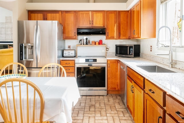 kitchen with under cabinet range hood, a sink, appliances with stainless steel finishes, decorative backsplash, and brown cabinets