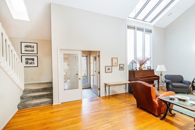 interior space with high vaulted ceiling, a skylight, baseboards, stairs, and light wood-style floors