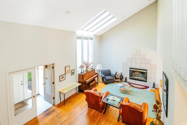 living area featuring high vaulted ceiling, a skylight, a fireplace, and wood finished floors