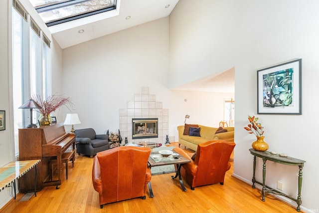 living area with a skylight, a fireplace, high vaulted ceiling, and light wood-style floors