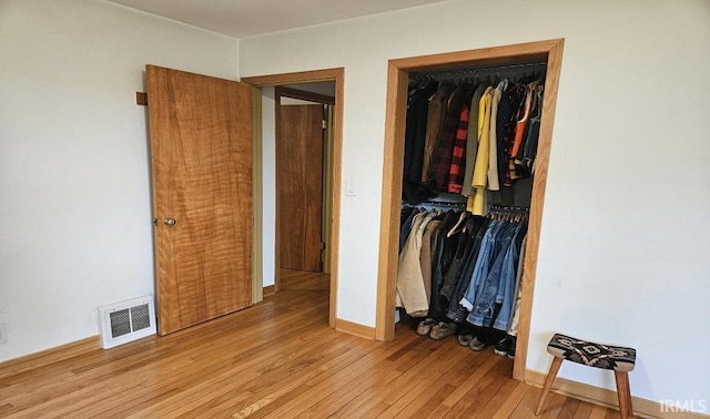 unfurnished bedroom featuring hardwood / wood-style flooring, a closet, visible vents, and baseboards