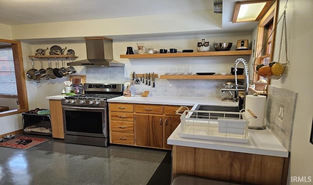 kitchen with open shelves, granite finish floor, brown cabinetry, stainless steel gas range oven, and wall chimney exhaust hood