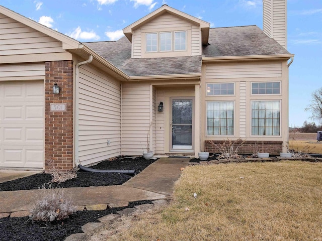 doorway to property featuring a garage, a shingled roof, a chimney, a yard, and brick siding