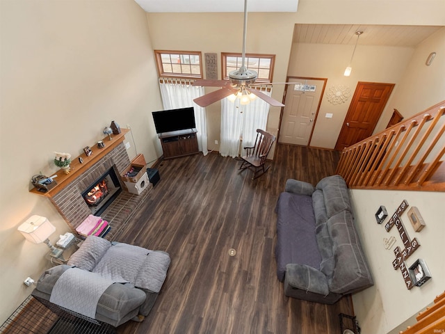 living area featuring ceiling fan, wood finished floors, a high ceiling, stairs, and a brick fireplace