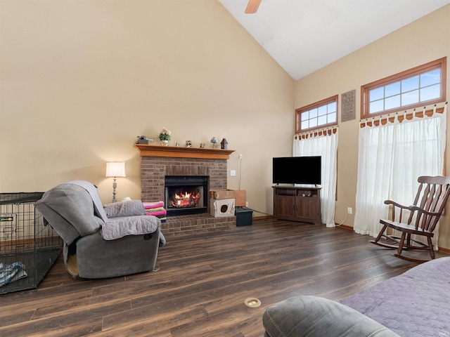 living area with ceiling fan, high vaulted ceiling, a brick fireplace, and wood finished floors