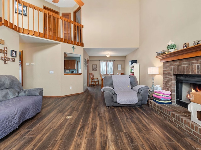 living area with a fireplace, a towering ceiling, a ceiling fan, wood finished floors, and baseboards