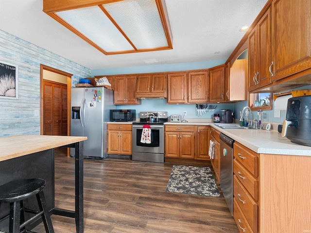 kitchen with a sink, light countertops, appliances with stainless steel finishes, brown cabinets, and wallpapered walls