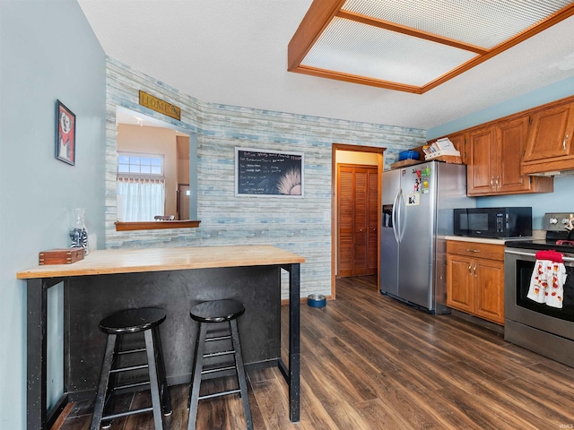 kitchen with dark wood-style floors, a breakfast bar area, stainless steel appliances, brown cabinetry, and wallpapered walls