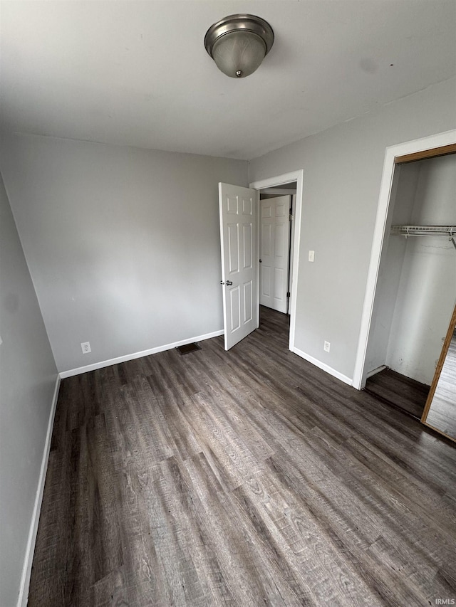 unfurnished bedroom featuring dark wood-type flooring, a closet, and baseboards