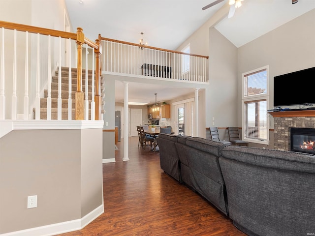 living room with high vaulted ceiling, ceiling fan with notable chandelier, a fireplace, stairs, and dark wood-style floors