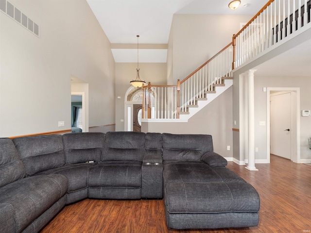 living area with decorative columns, visible vents, a towering ceiling, stairway, and wood finished floors