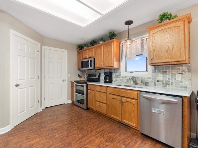 kitchen with stainless steel appliances, a sink, light countertops, backsplash, and dark wood finished floors