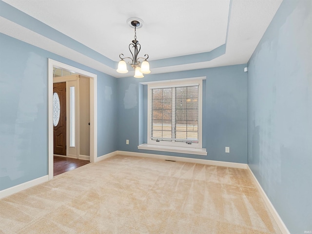 unfurnished room with a notable chandelier, a tray ceiling, carpet flooring, and baseboards