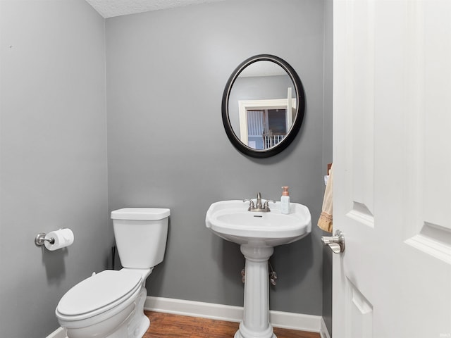 half bath featuring wood finished floors, toilet, and baseboards