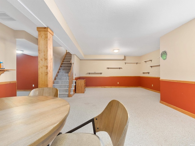 carpeted dining room featuring a textured ceiling, visible vents, baseboards, stairs, and ornate columns