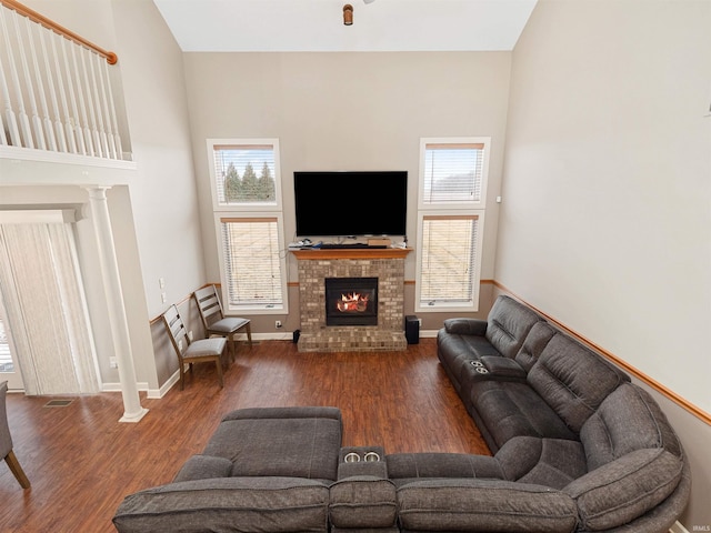 living area featuring a brick fireplace, a high ceiling, baseboards, and wood finished floors