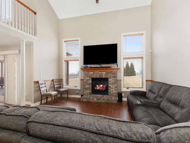 living area with a fireplace, decorative columns, wood finished floors, high vaulted ceiling, and baseboards