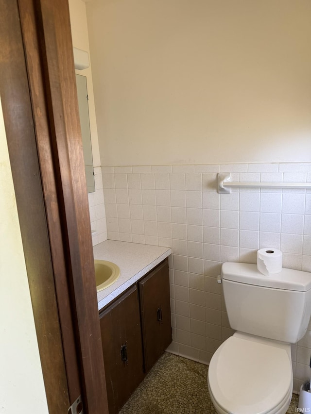 bathroom with toilet, a wainscoted wall, vanity, and tile walls