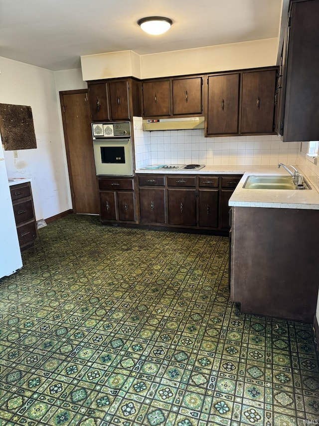 kitchen with white appliances, a sink, under cabinet range hood, and decorative backsplash