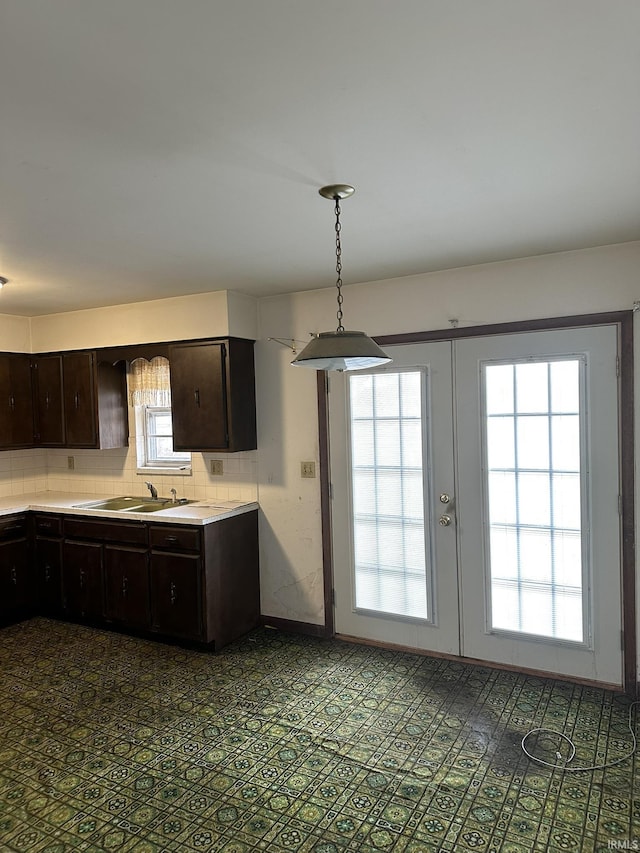 kitchen featuring dark brown cabinetry, a sink, light countertops, french doors, and tasteful backsplash