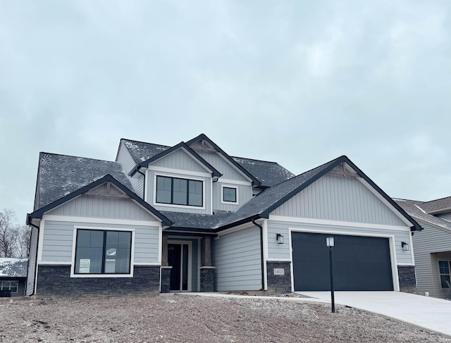 view of front of house featuring a shingled roof, concrete driveway, an attached garage, board and batten siding, and stone siding