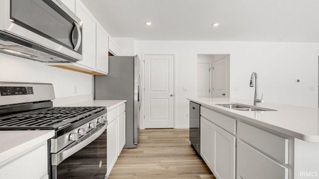 kitchen with light countertops, appliances with stainless steel finishes, light wood-style floors, white cabinets, and a sink