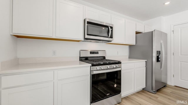 kitchen featuring stainless steel appliances, light countertops, white cabinetry, and light wood-style floors