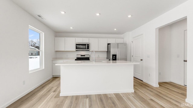 kitchen featuring a center island with sink, appliances with stainless steel finishes, light countertops, light wood-style floors, and a sink