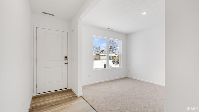 entrance foyer with light wood finished floors, baseboards, visible vents, and light colored carpet