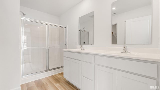 full bath featuring a stall shower, double vanity, a sink, and wood finished floors